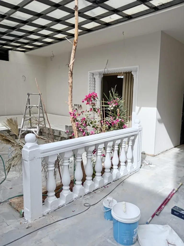 أعمال دهانات خارجية جارية لواجهة منزل، تشمل طلاء سور وبلكونة باللون الأبيض