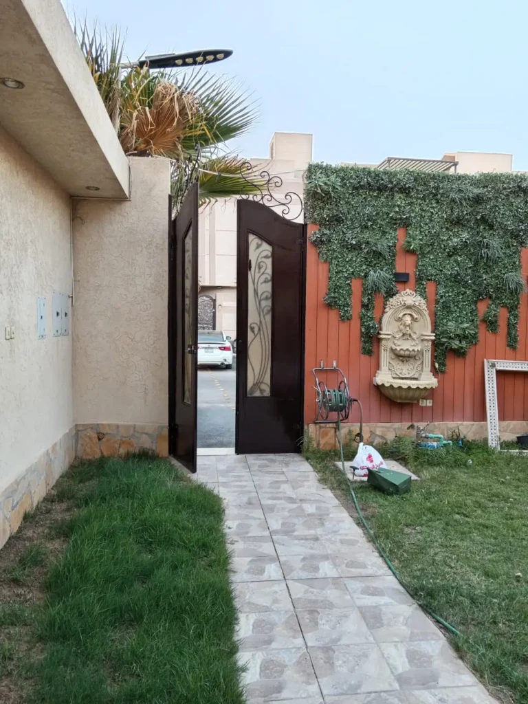 باب خارجي حديدي مطلي بالبني الغامق في حديقة منزلية في الرياض مع جدار ديكور عشبي
